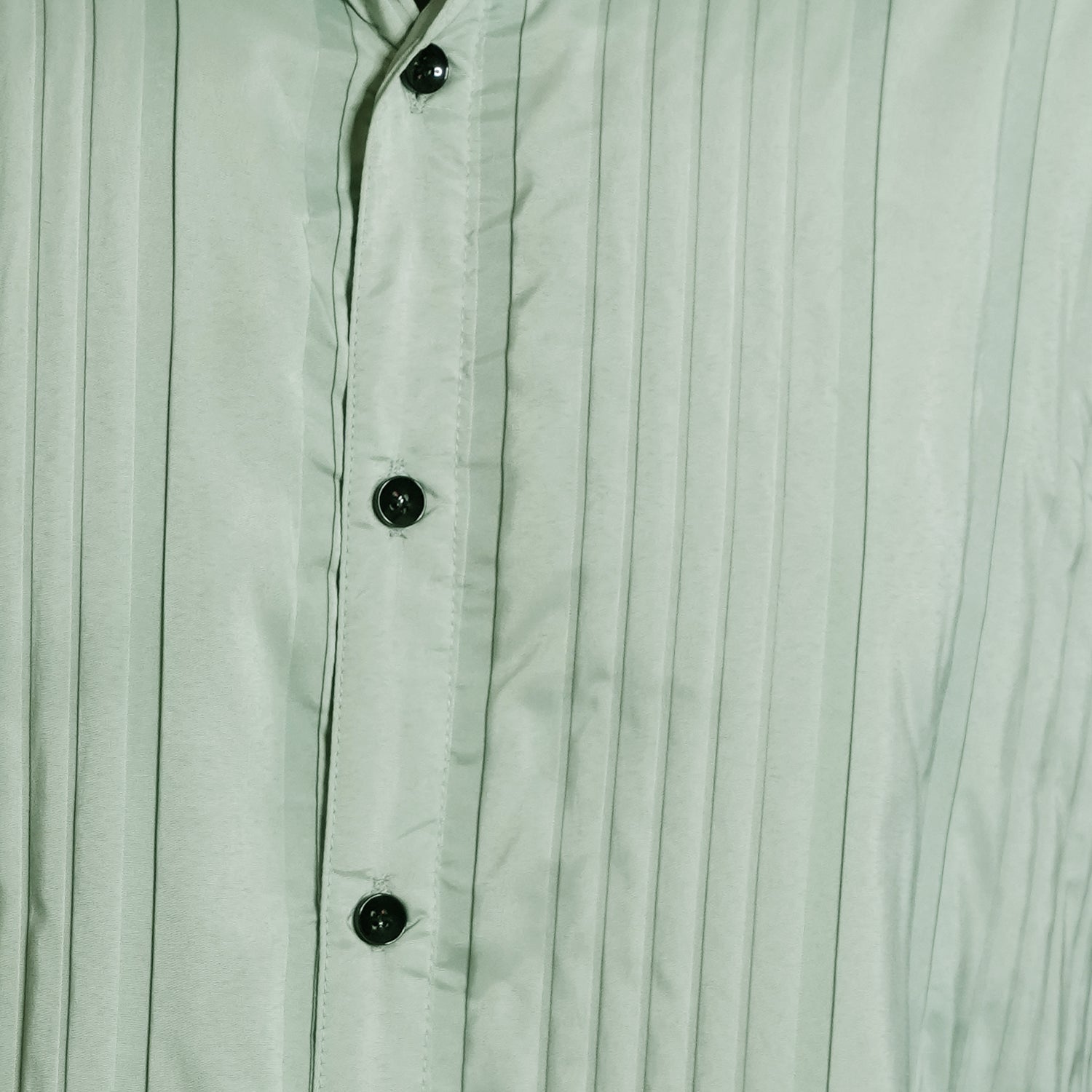 Close-up of a light green button-up shirt with vertical pleats.