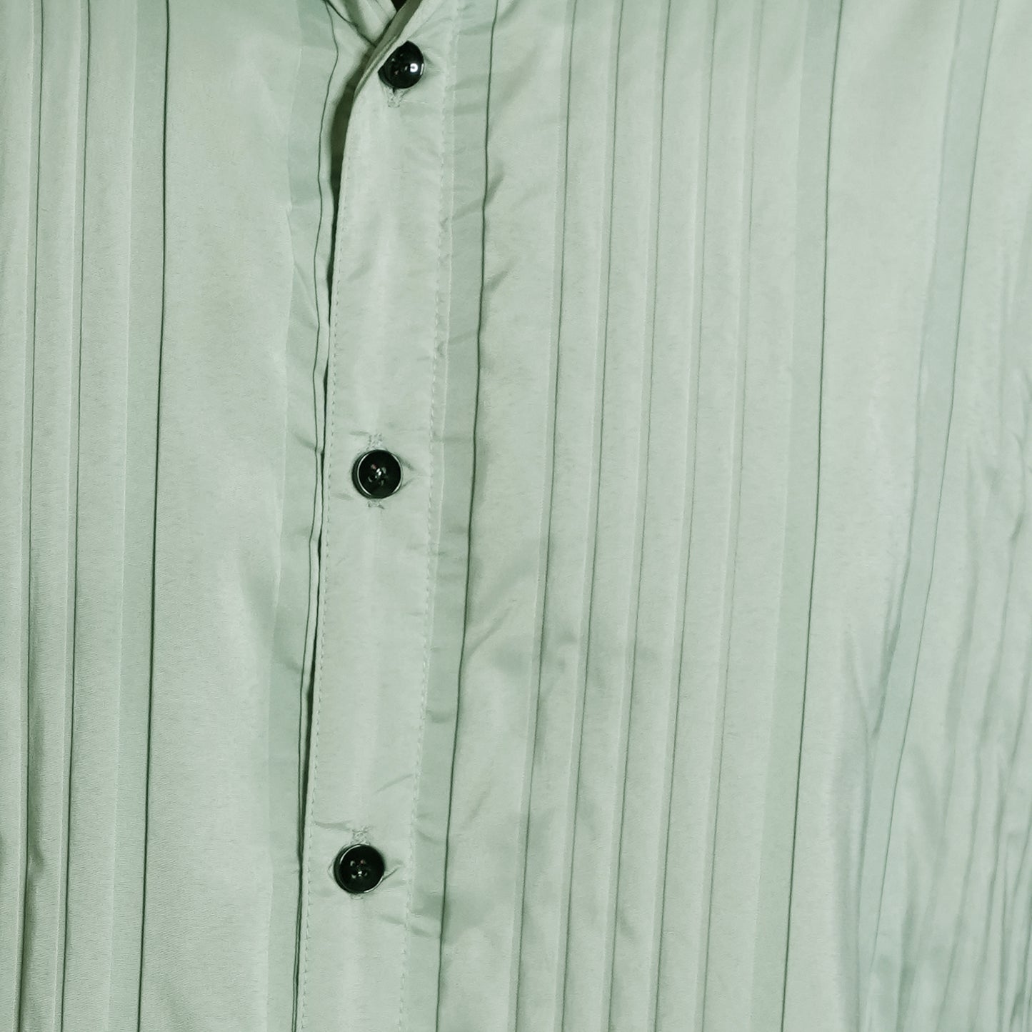 Close-up of a light green button-up shirt with vertical pleats.